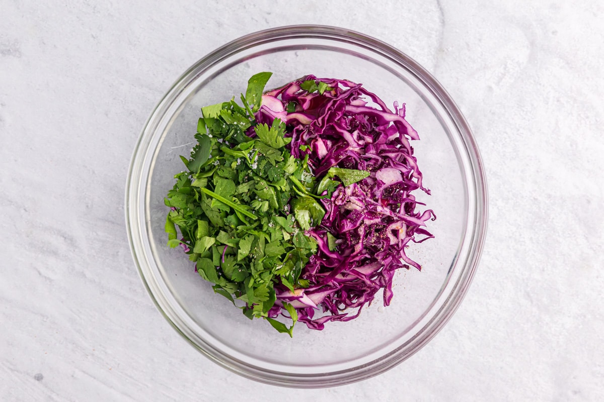 Combining shredded cabbage and cilantro in a glass bowl.