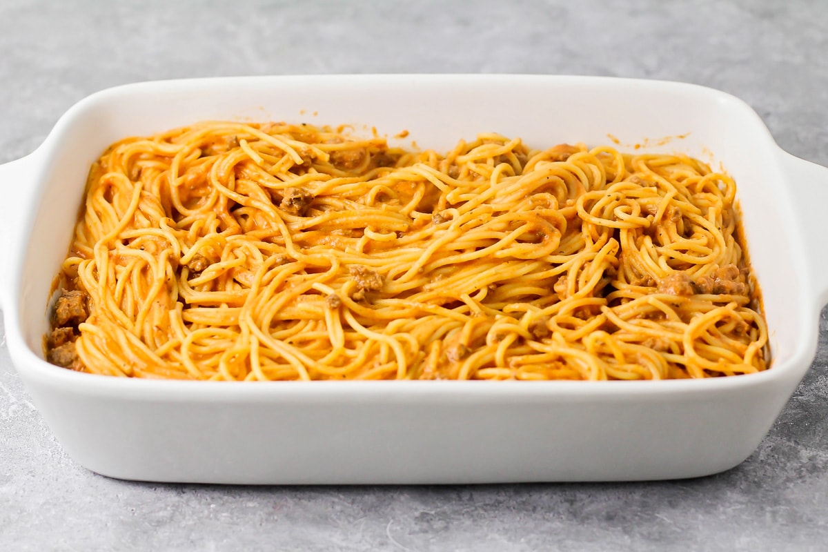 Spaghetti noodles and meat mixed together and poured into baking dish.