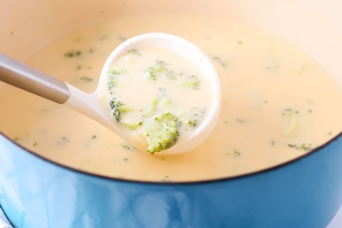 Scooping broccoli cheese soup from a pot.