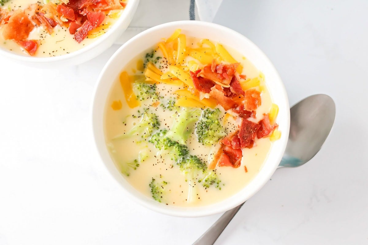 A bowl of broccoli cheese soup topped with bacon and shredded cheese.