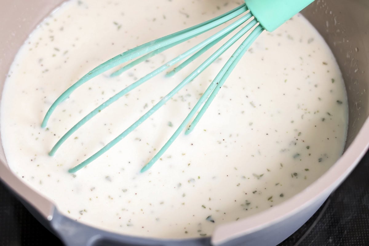 Whisking roux and milk mixture in a pot for cheese sauce.