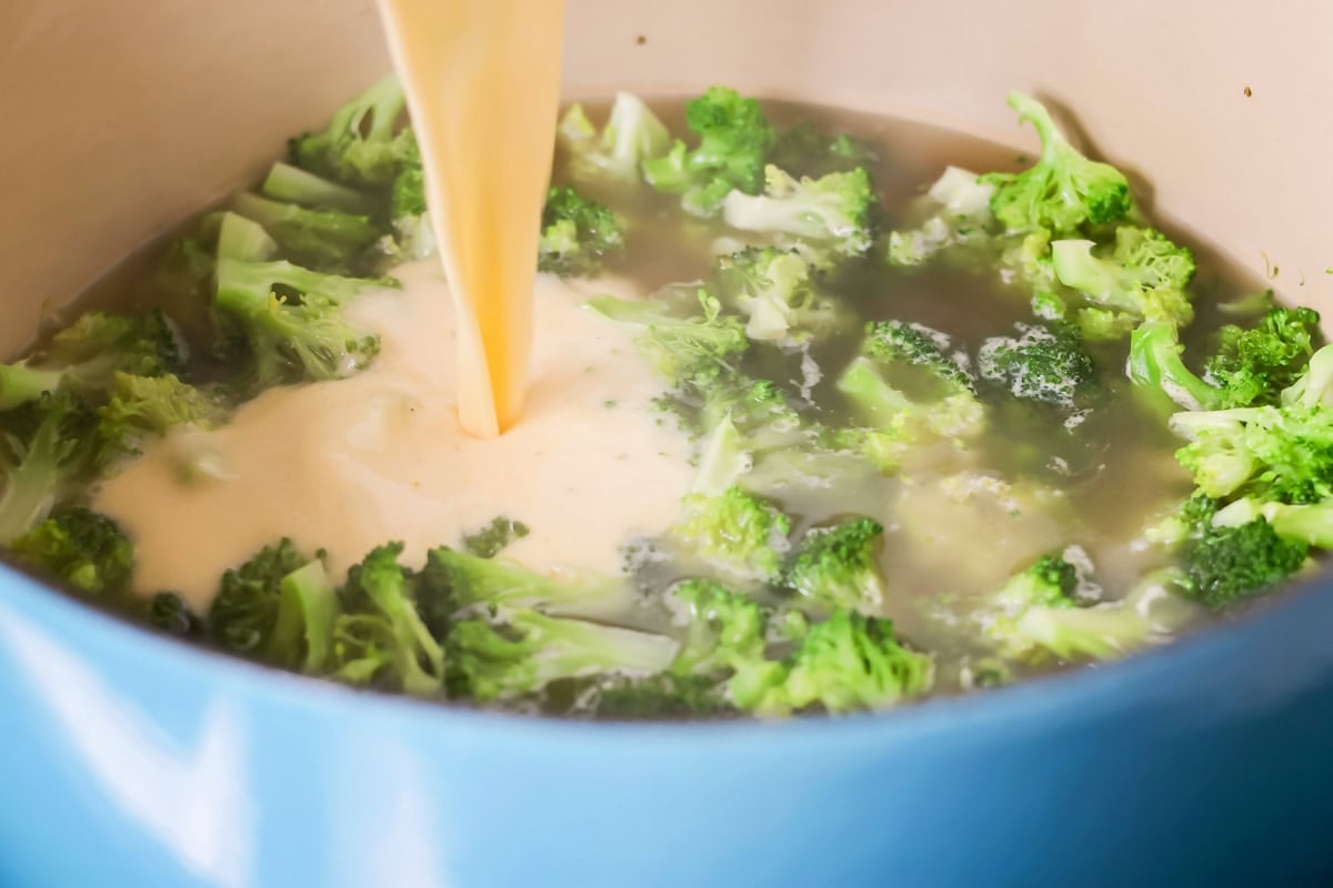 Adding cheese sauce to broccoli cheese soup.