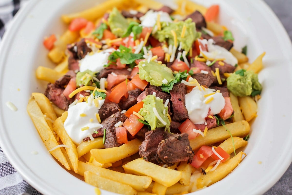 Top view of a plate of carne asada fries topped with sour cream and guacamole.