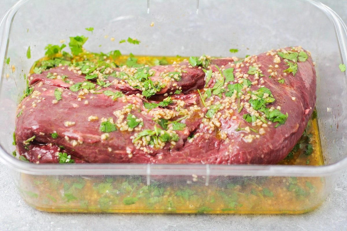 Coating steak with marinade in a glass baking dish.