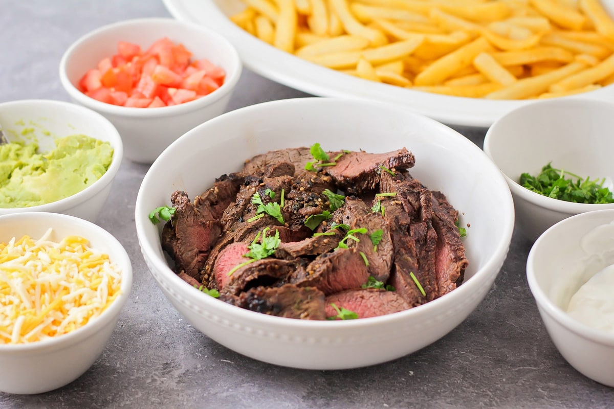 Carne asada, fries, and other ingredients in a variety of bowls on a counter.