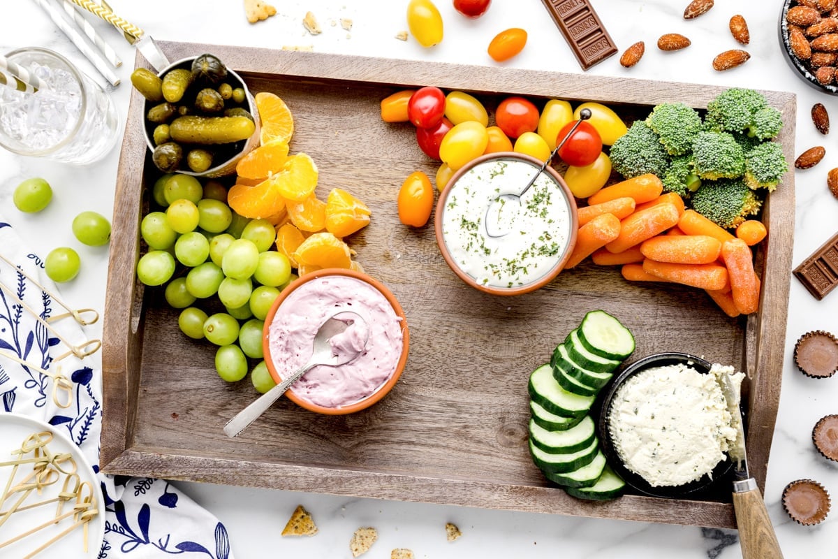 Placing fruit onto a wooden board of dips and veggies.