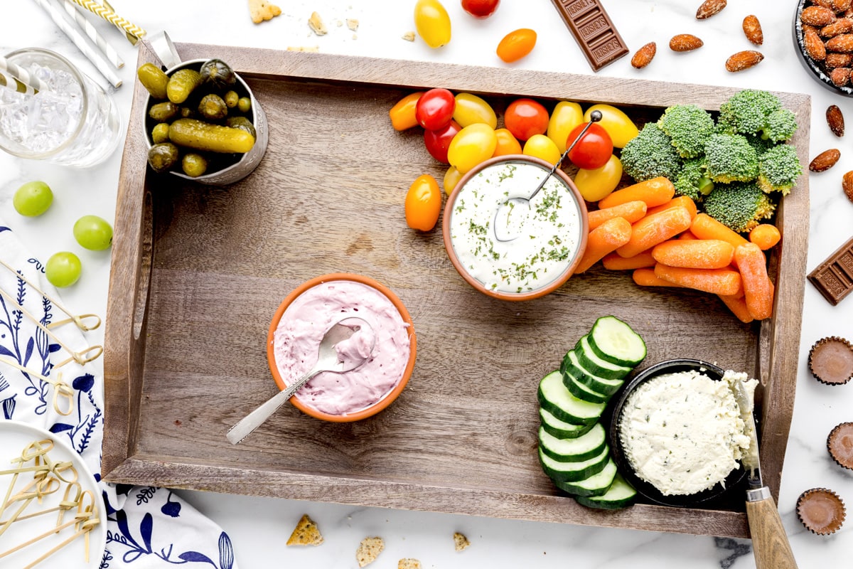 Laying veggies around bowls of dips on a wooden board.