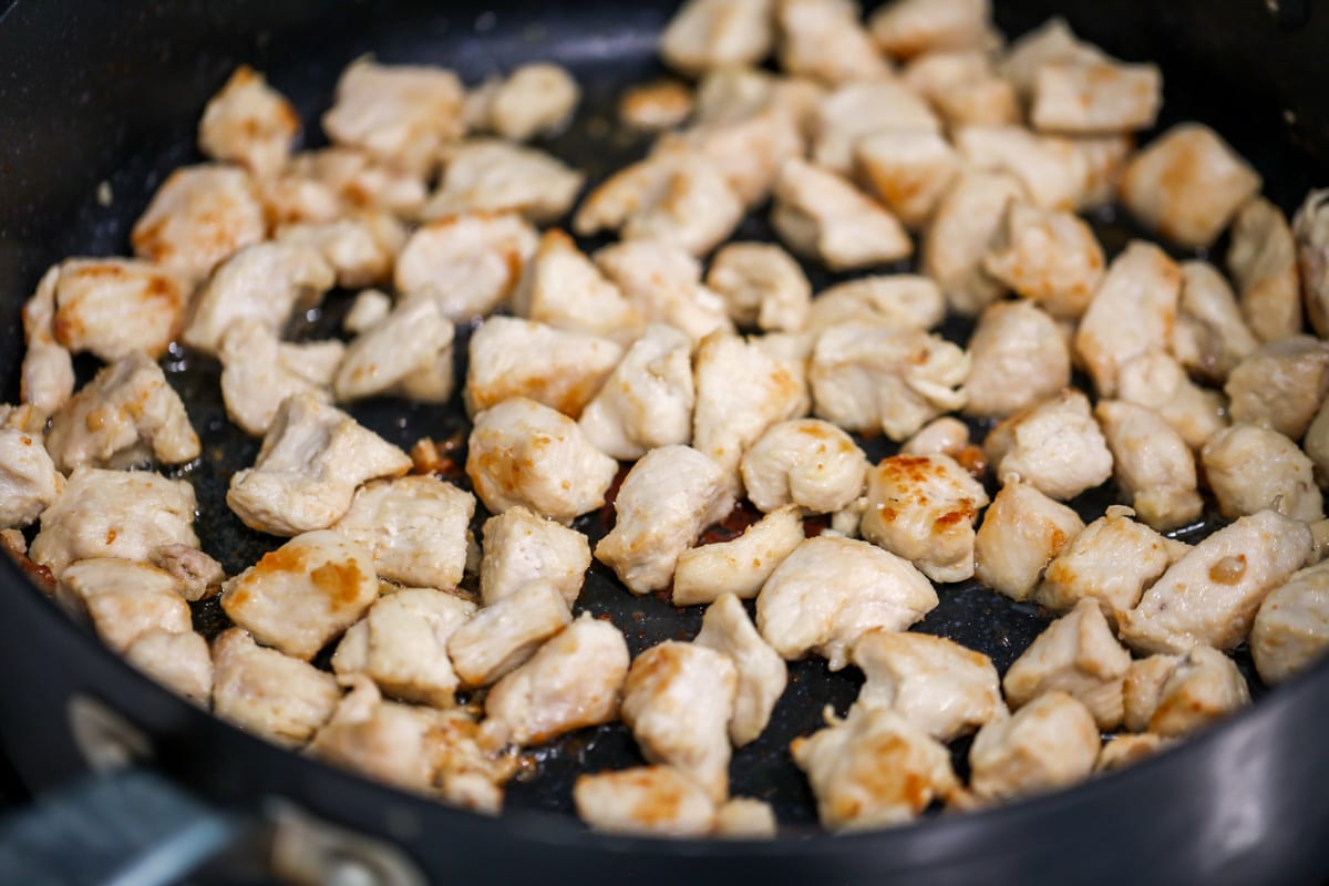 Chicken pieces cooking in a pan on the stove.