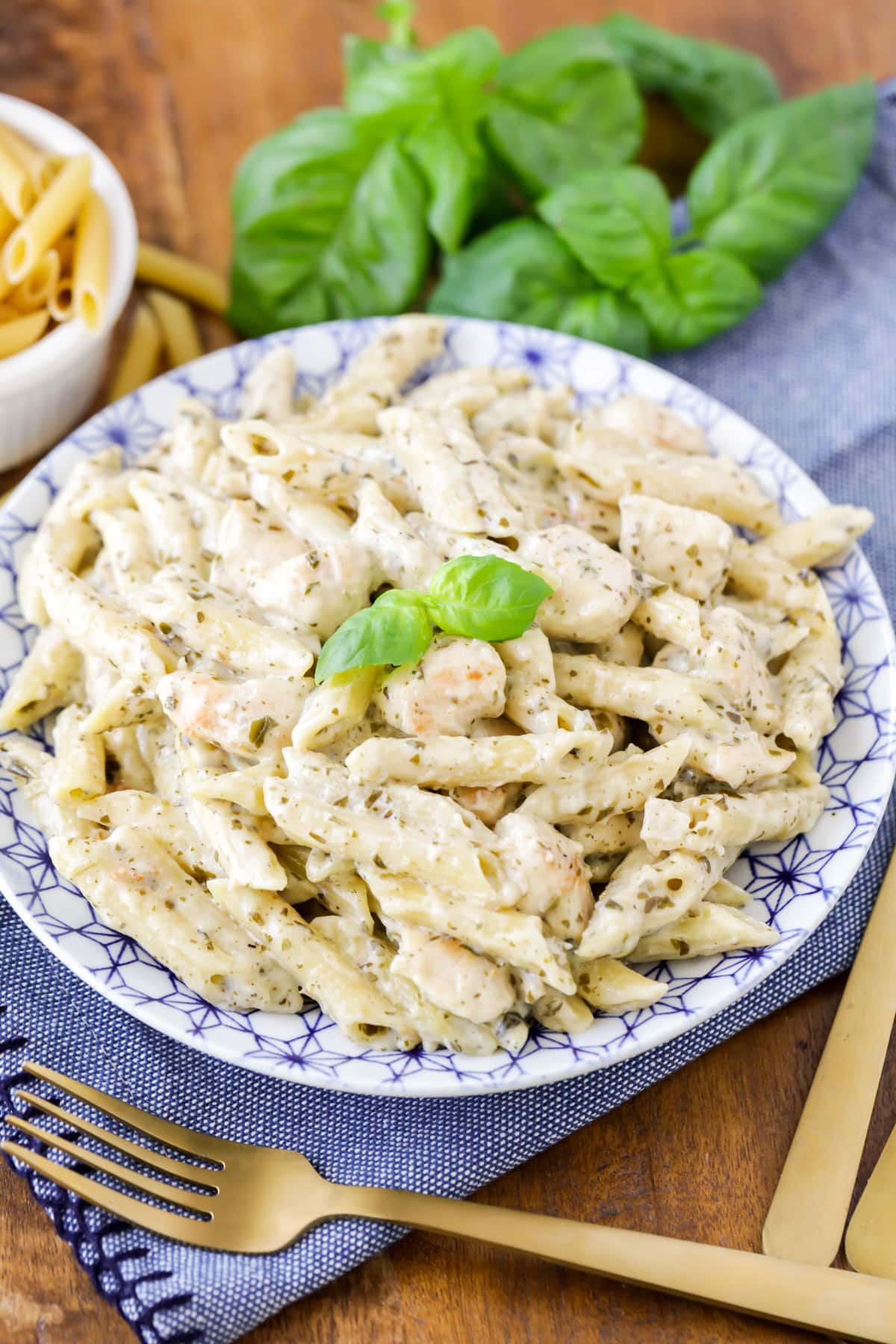 A plate filled with chicken pesto pasta topped with fresh basil.