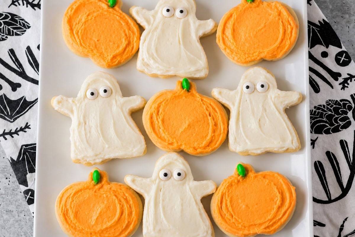 Halloween sugar cookies decorated as ghosts and pumpkins on white platter.
