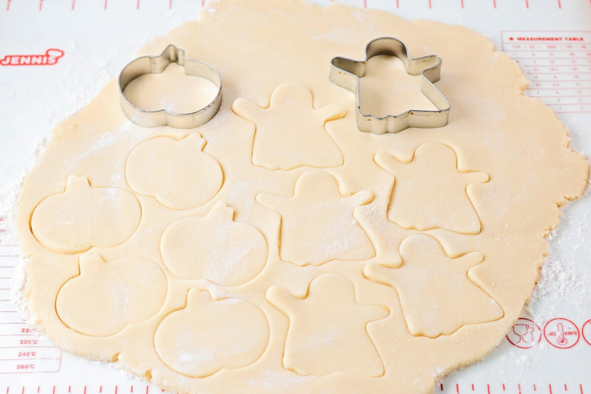 Ghosts and pumpkins being cut out of sugar cookie dough.
