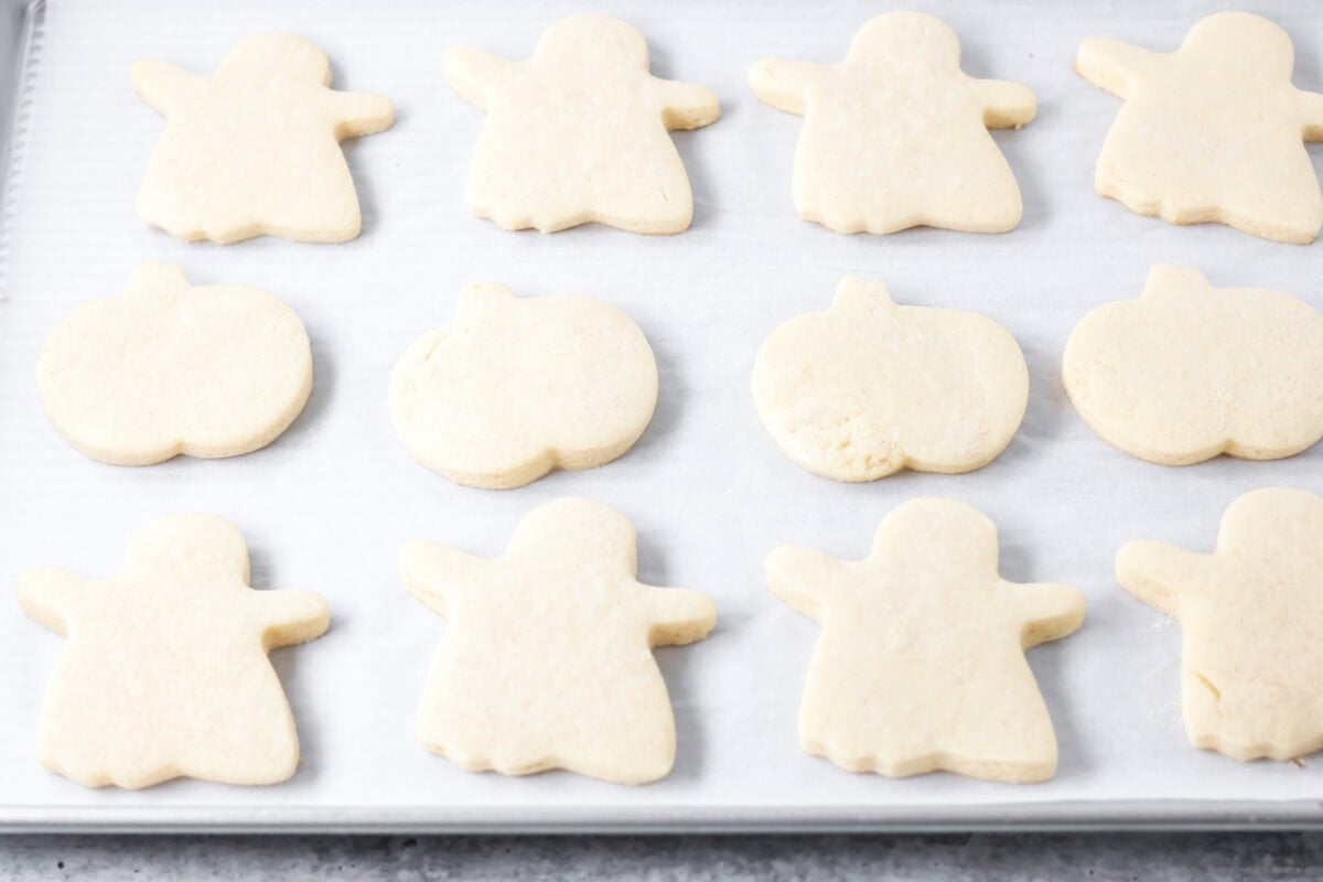 Ghost and pumpkin sugar cookies on parchment paper lined cookie sheet.