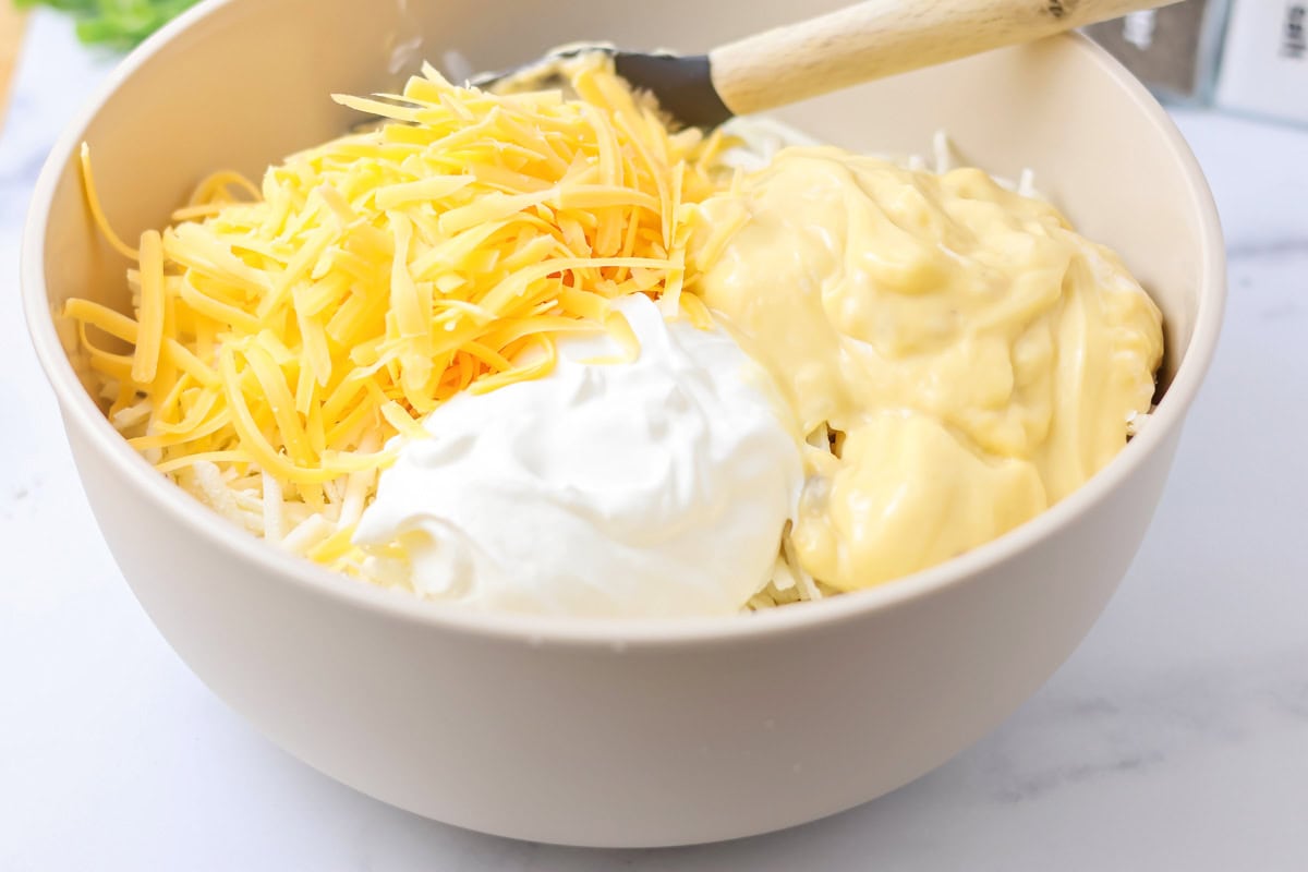 Hashbrowns, bacon, soup, sour cream and cheese in bowl.