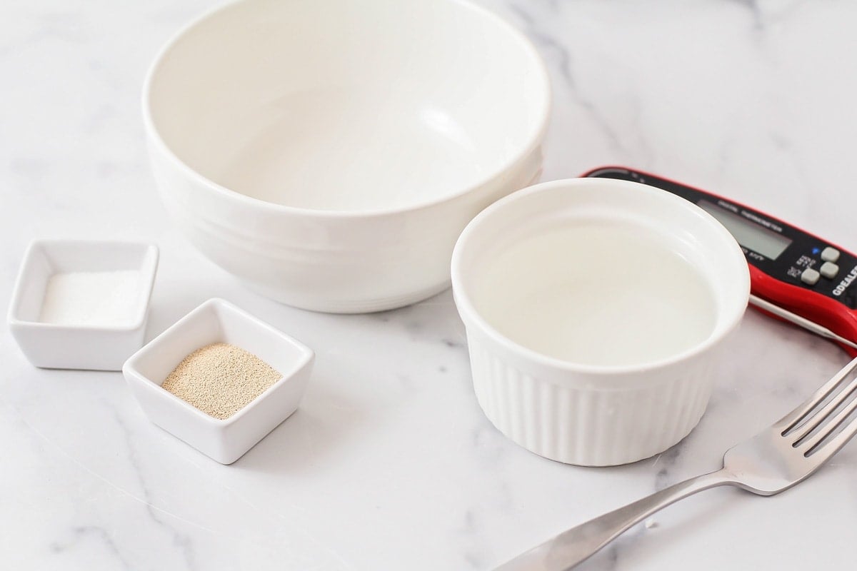 Two white bowls, a bowl of yeast and sugar on a kitchen counter.