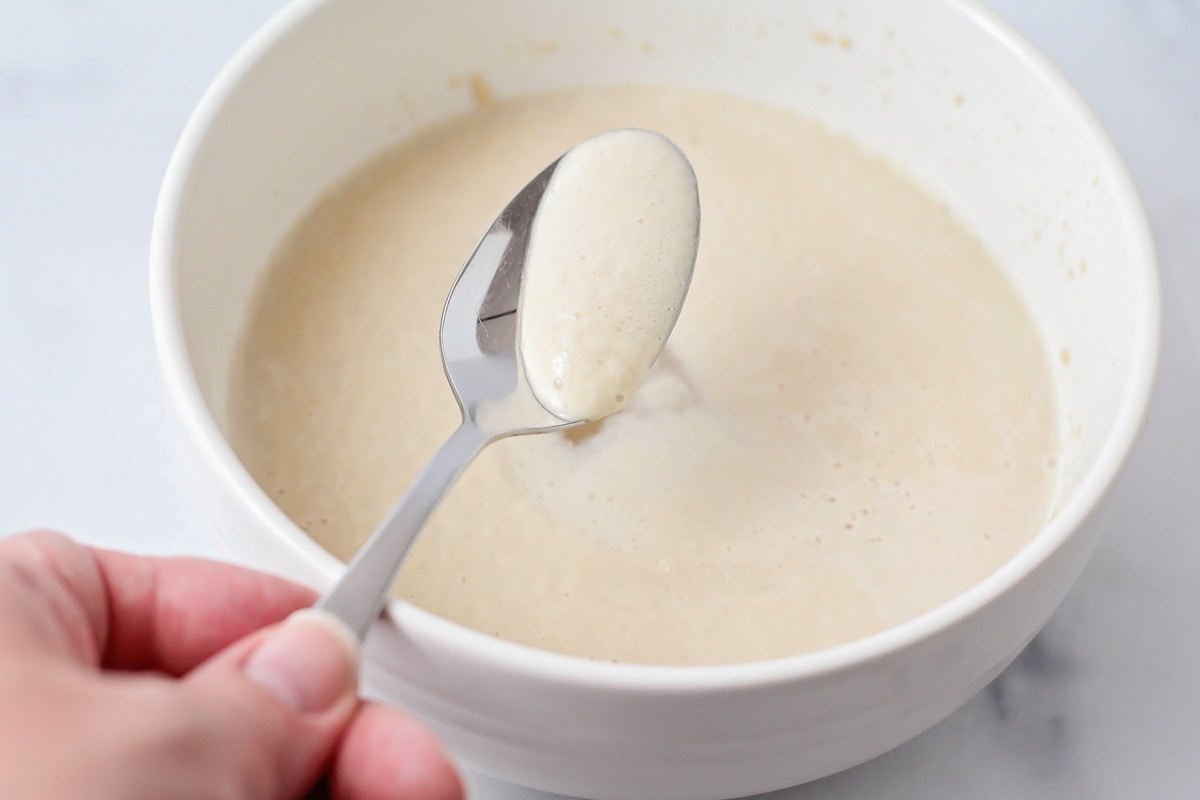 Close up of a spoon filled with activated yeast over a white bowl.