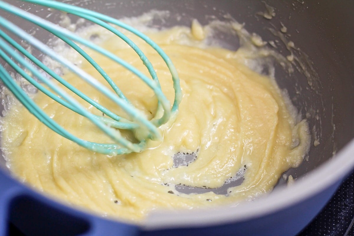 Whisking a mixture of melted butter and flour in a pot on the stove.