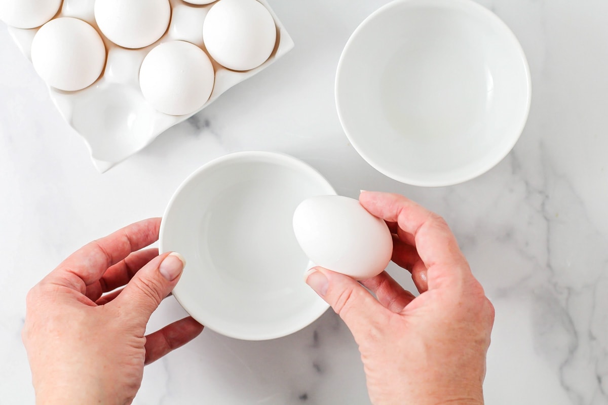 Two white bowls with an egg in a hand above it.