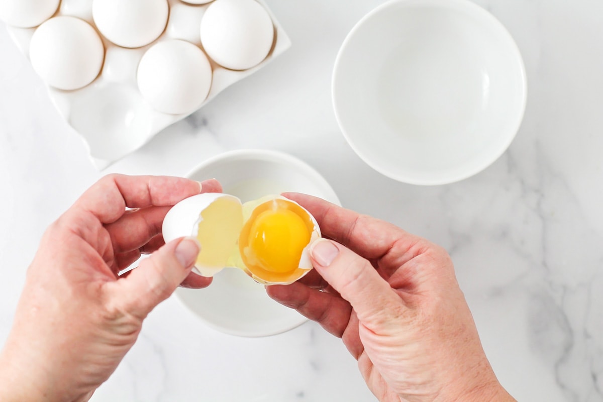 Two white bowls with hands cracking an egg above it.