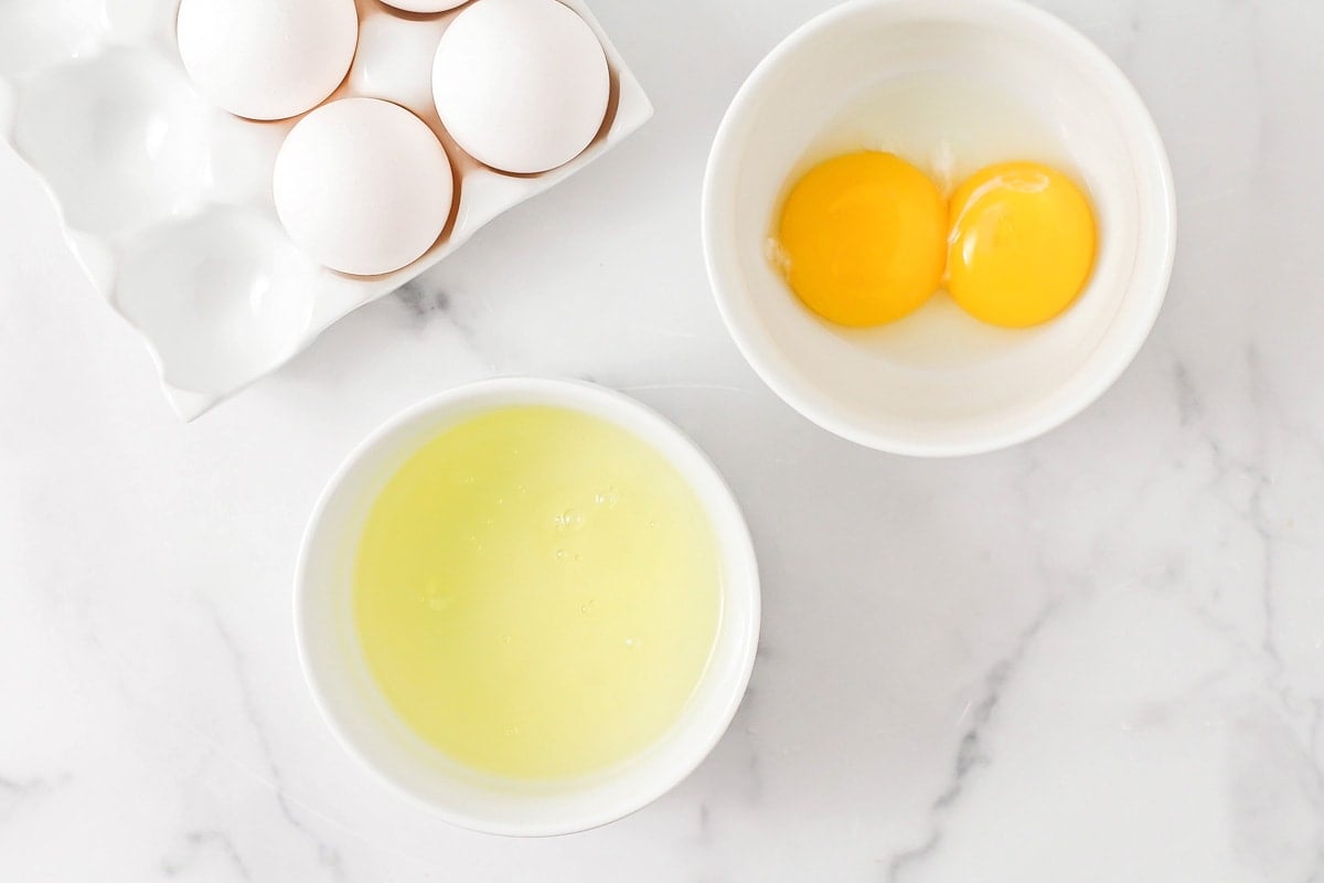 Two white bowls with egg whites in one and yolks in another.