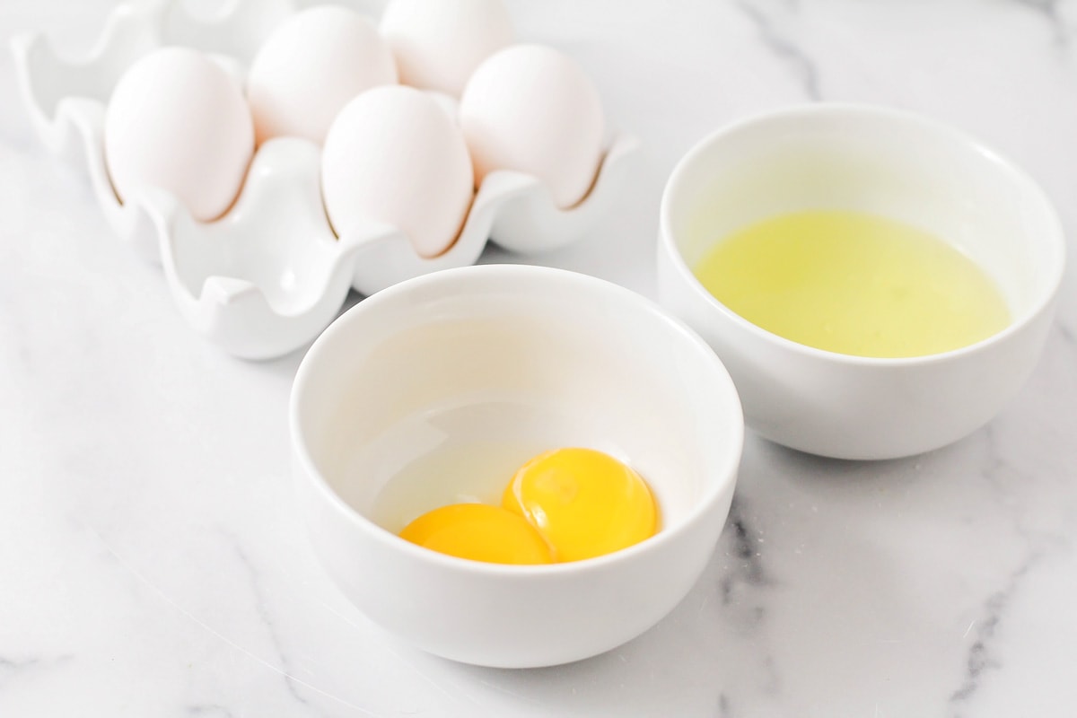 Two white bowls with egg whites and yolks.