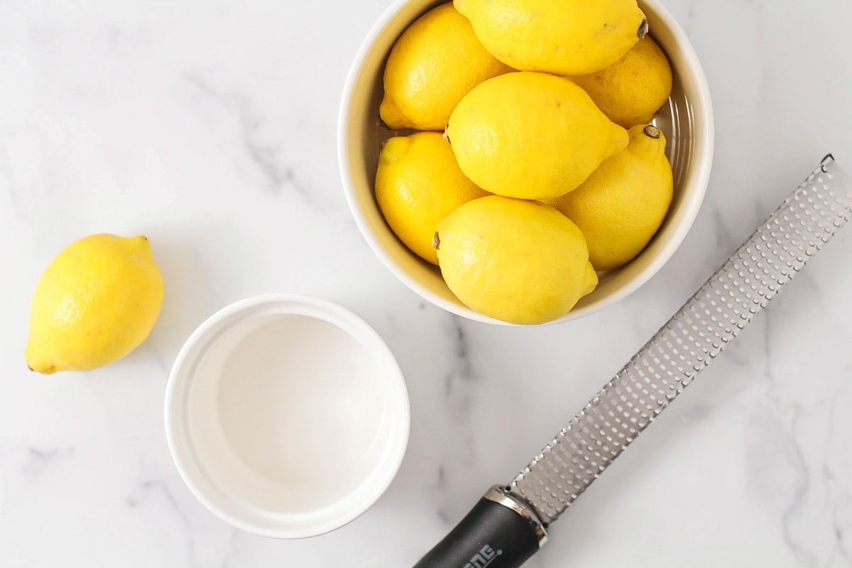 Lemons, a white bowl, and a zester all set on a kitchen counter.