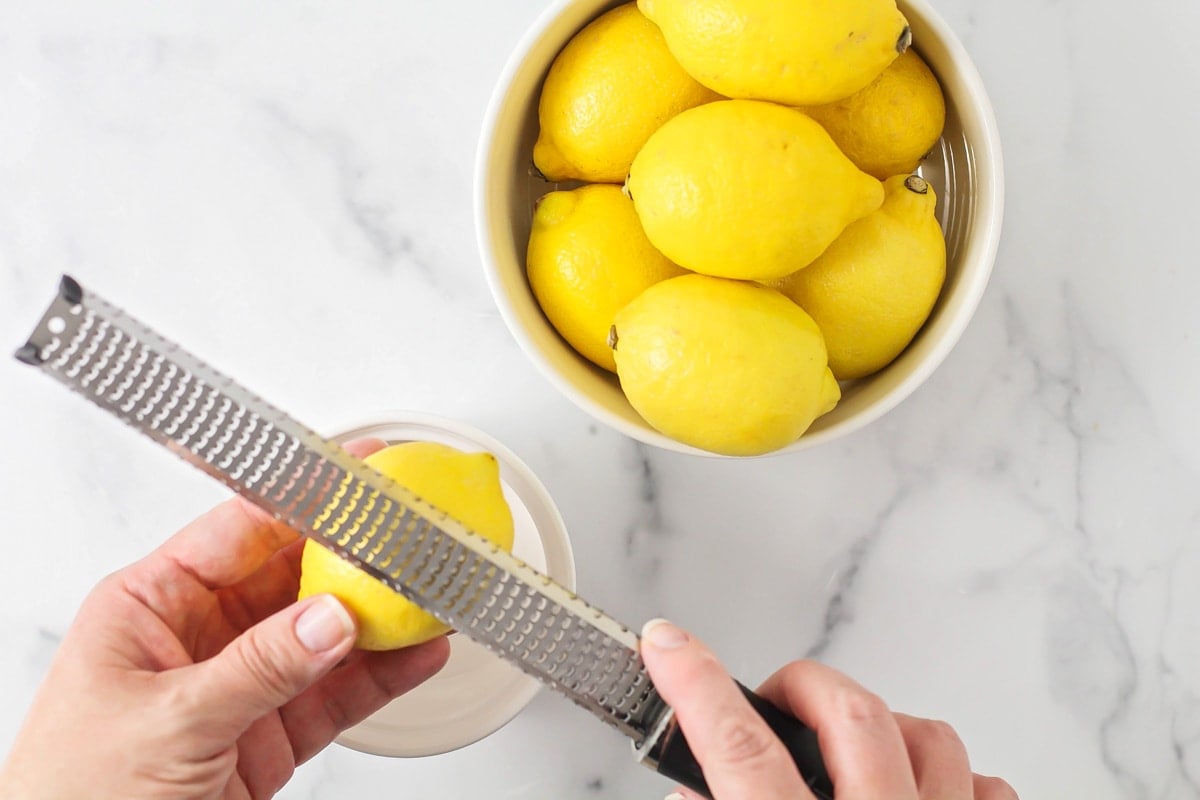 Zesting a lemon with a micro planer above a white bowl.