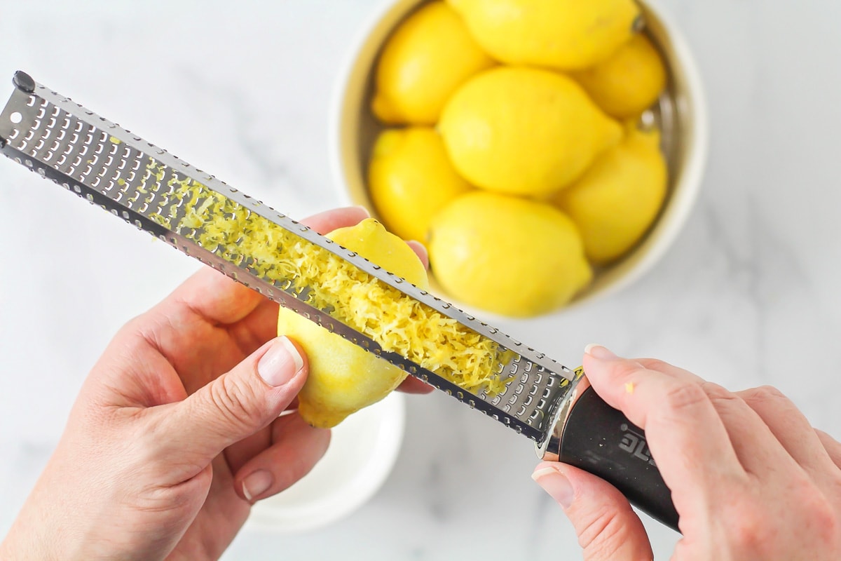 A micro planer filled with lemon zest above a white bowl.
