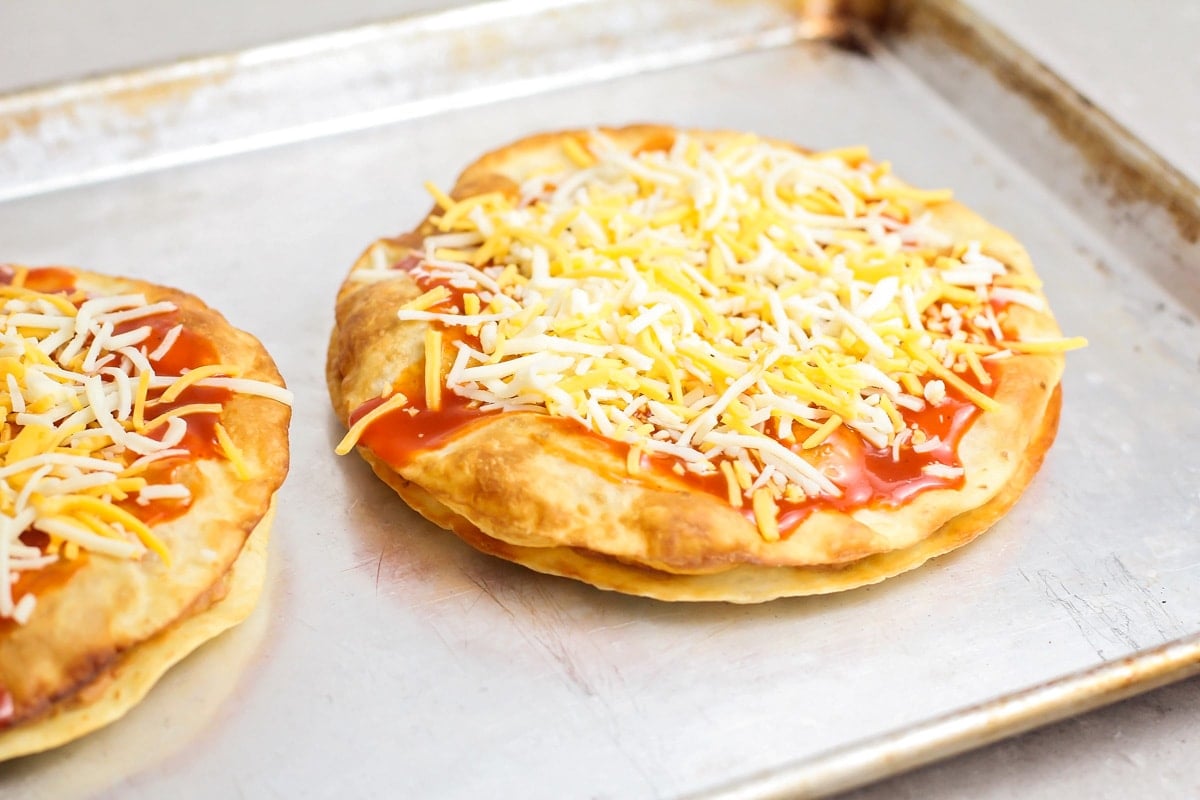 Two tortilla pizzas topped with cheese and ready to be baked.