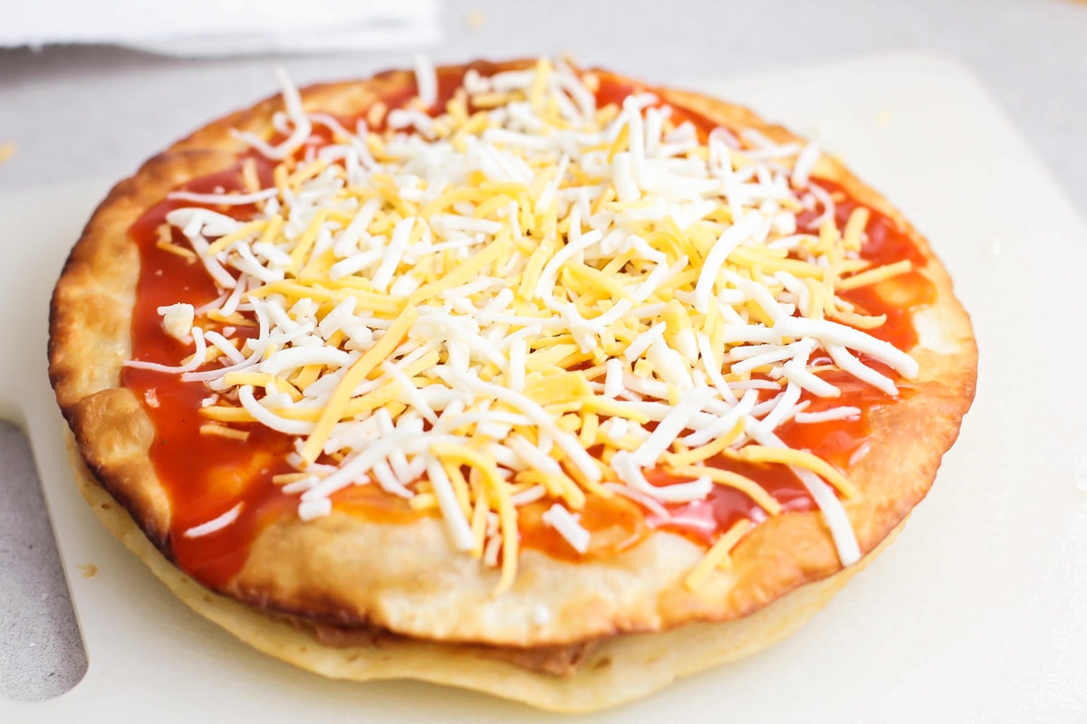 Two tortilla pizzas topped with cheese and ready to be baked.