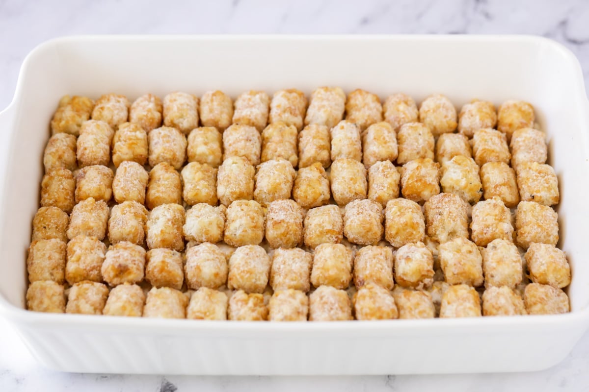 Tater tots layered on top of a veggie mixture in a white baking dish.