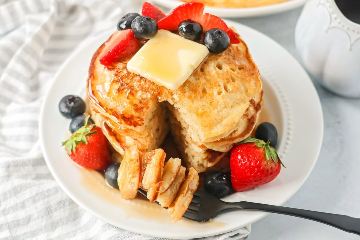 A stack of buttermilk pancakes topped with butter, syrup, and fresh fruit.