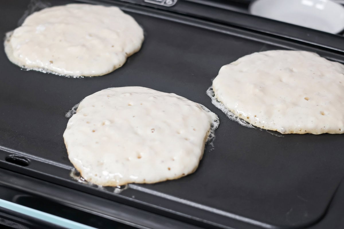 Buttermilk pancakes cooking on a griddle.