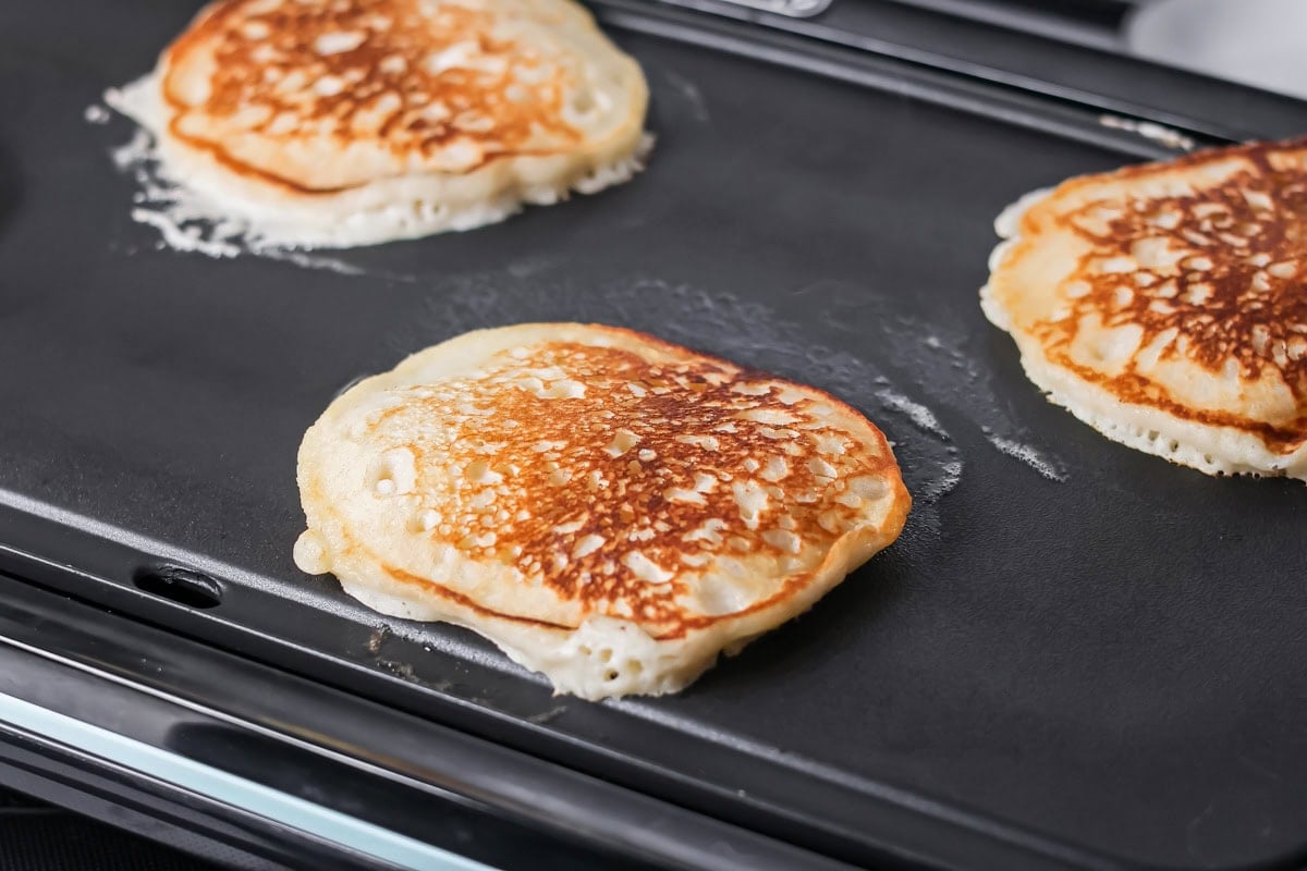 Buttermilk pancakes cooking on a griddle.