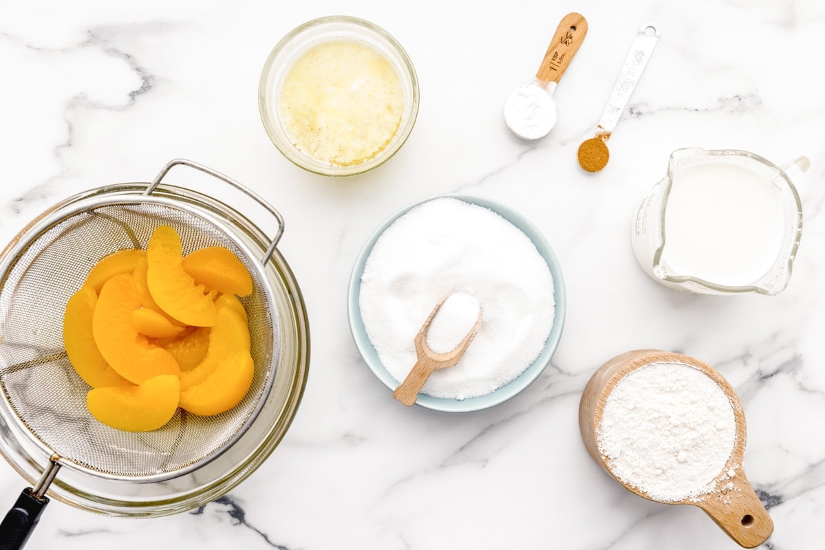 Peaches, sugar, flour, and other ingredients on a kitchen counter.