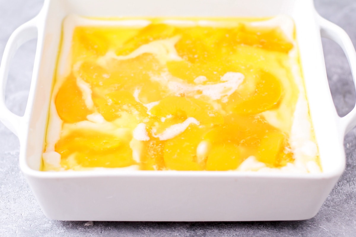 Canned peached poured over cobbler batter in baking dish.