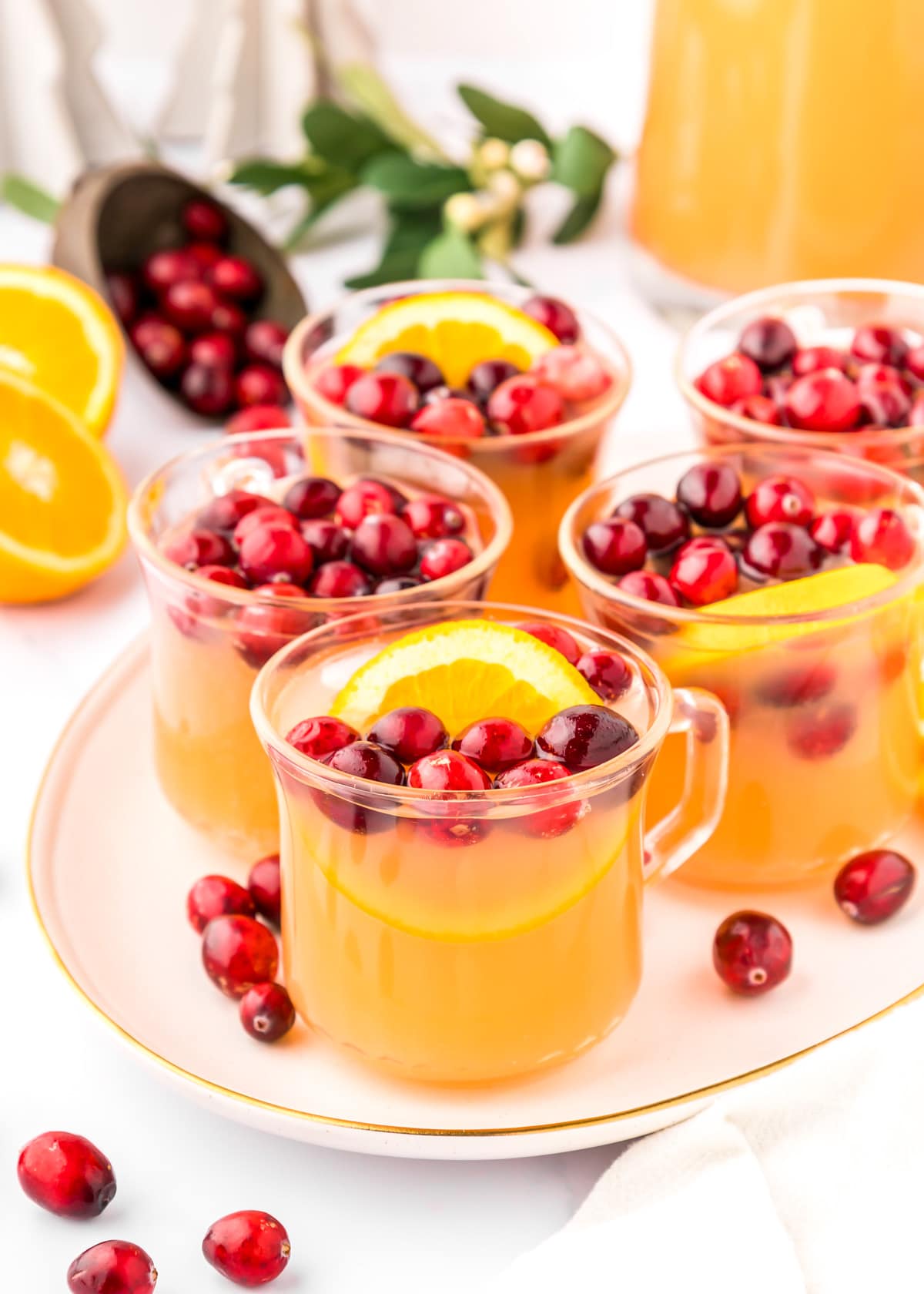 Glass cups filled with Christmas punch and topped with cranberries and orange slices.
