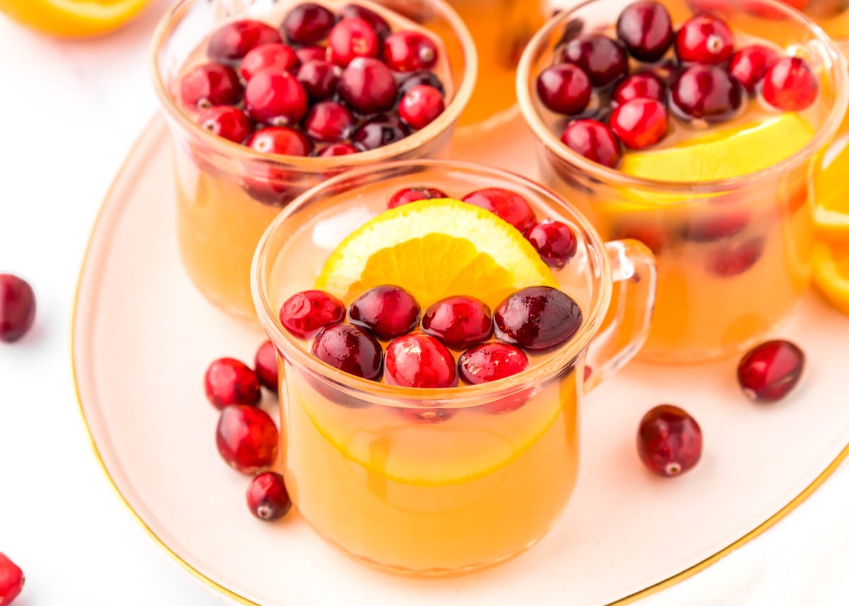 Cups of Christmas punch garnished with fresh cranberries and orange slices.
