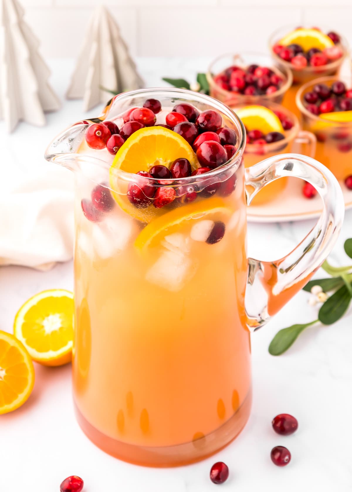 A glass pitcher filled with juice and garnished with cranberries and oranges.