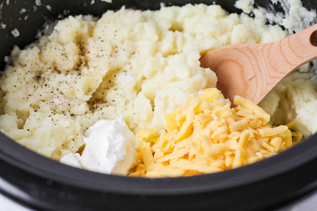 Adding cheese and sour cream to mashed potatoes in a crockpot.
