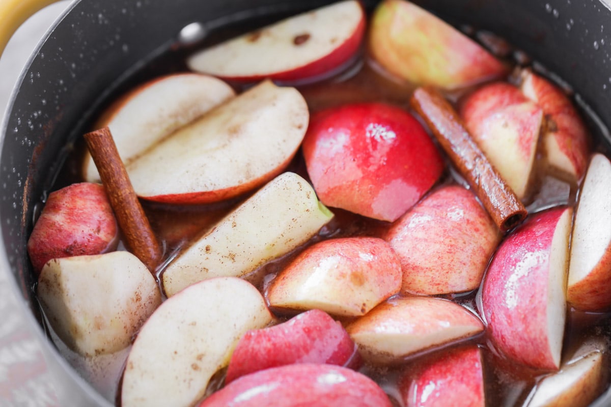 Quartered apples and seasonings cooking in a pot on the stove.