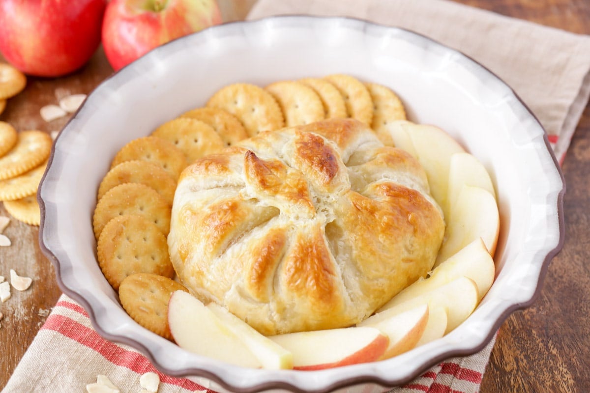 A baked brie in puff pastry served with crackers and apple slices.