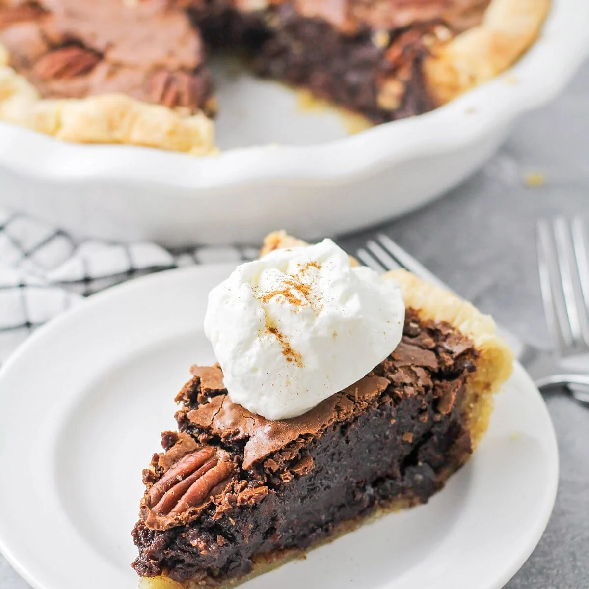 A slice of chocolate pecan pie topped with whipped cream.