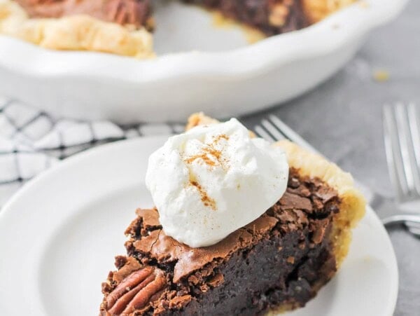 A slice of chocolate pecan pie topped with whipped cream.