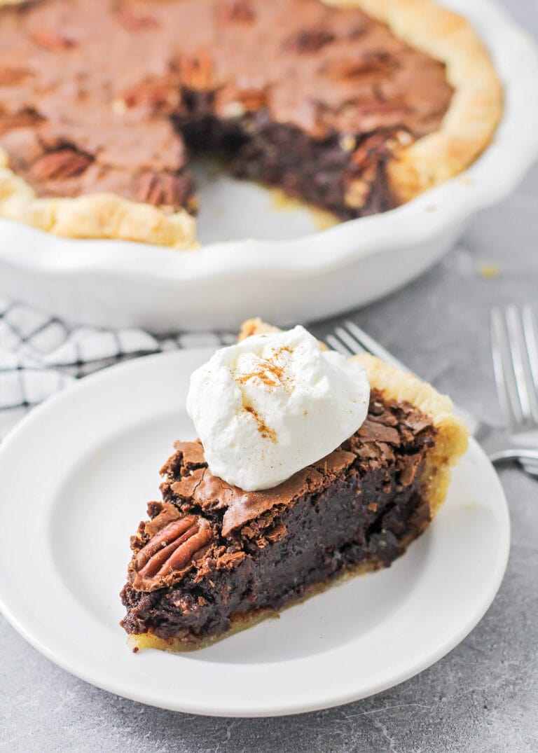 A slice of chocolate pecan pie topped with whipped cream.