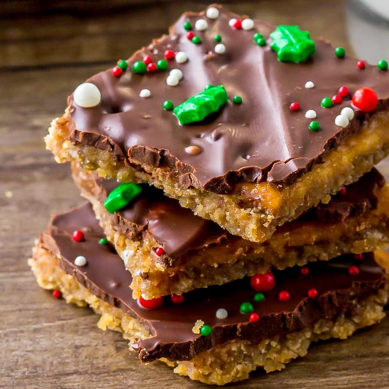 Close up of Christmas crack recipe stacked and topped with sprinkles.