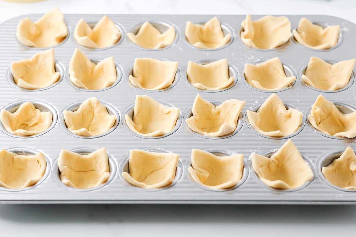 Placing crescent dough in a muffin tin for cranberry brie bites.