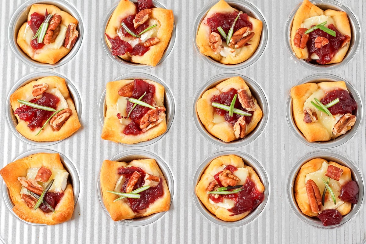 Cranberry brie bites in a cupcake pan topped with rosemary.