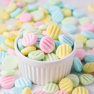 Homemade cream cheese mints in pastel colors in cup on counter.