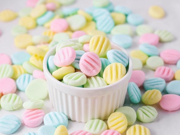 Homemade cream cheese mints in pastel colors in cup on counter.