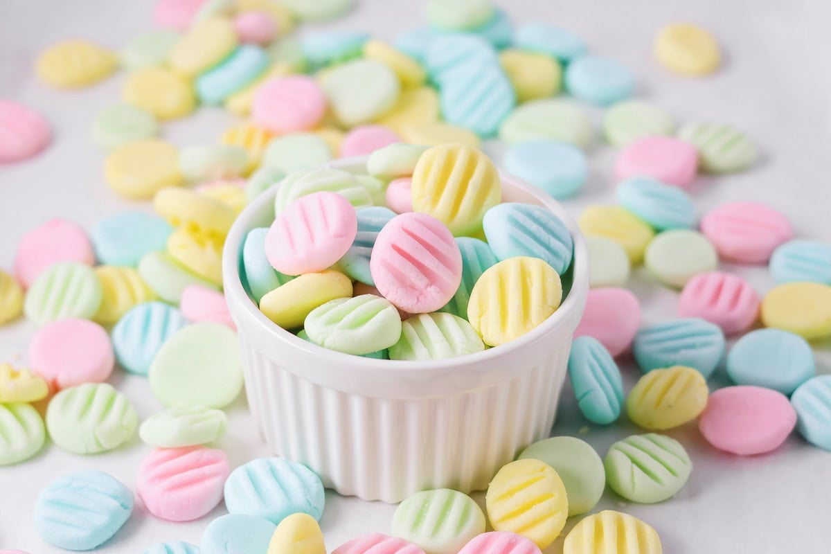 Homemade cream cheese mints in pastel colors in cup on counter.